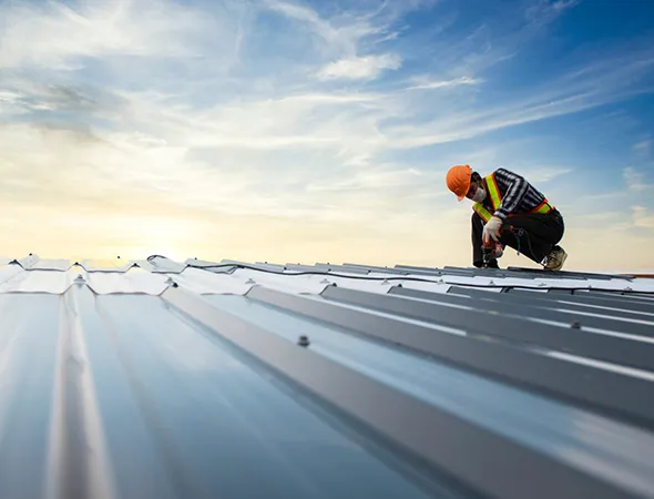 A man is installing metal roofing, showcasing expertise in commercial roofing techniques and safety practices.