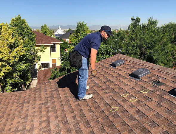 A man stands on a roof, using a ladder for roofing work, demonstrating safety and skill in his task.