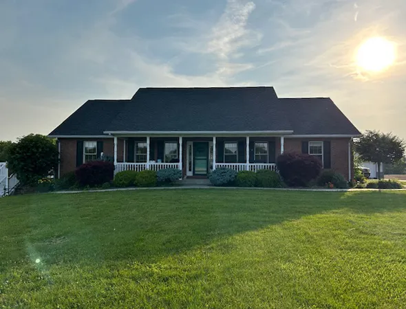A brick house with a spacious yard under bright sunlight, showcasing a well-maintained roofing structure.