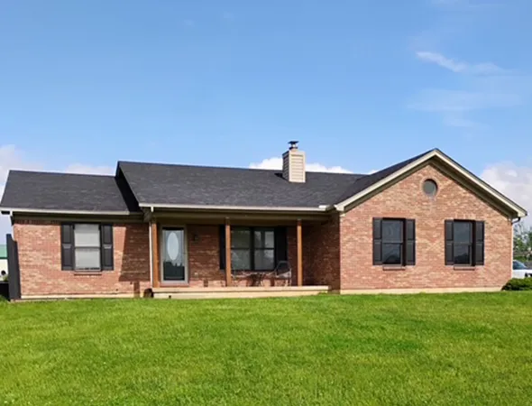 A brick house featuring a spacious yard and driveway, showcasing a well-maintained roofing structure above the entrance.